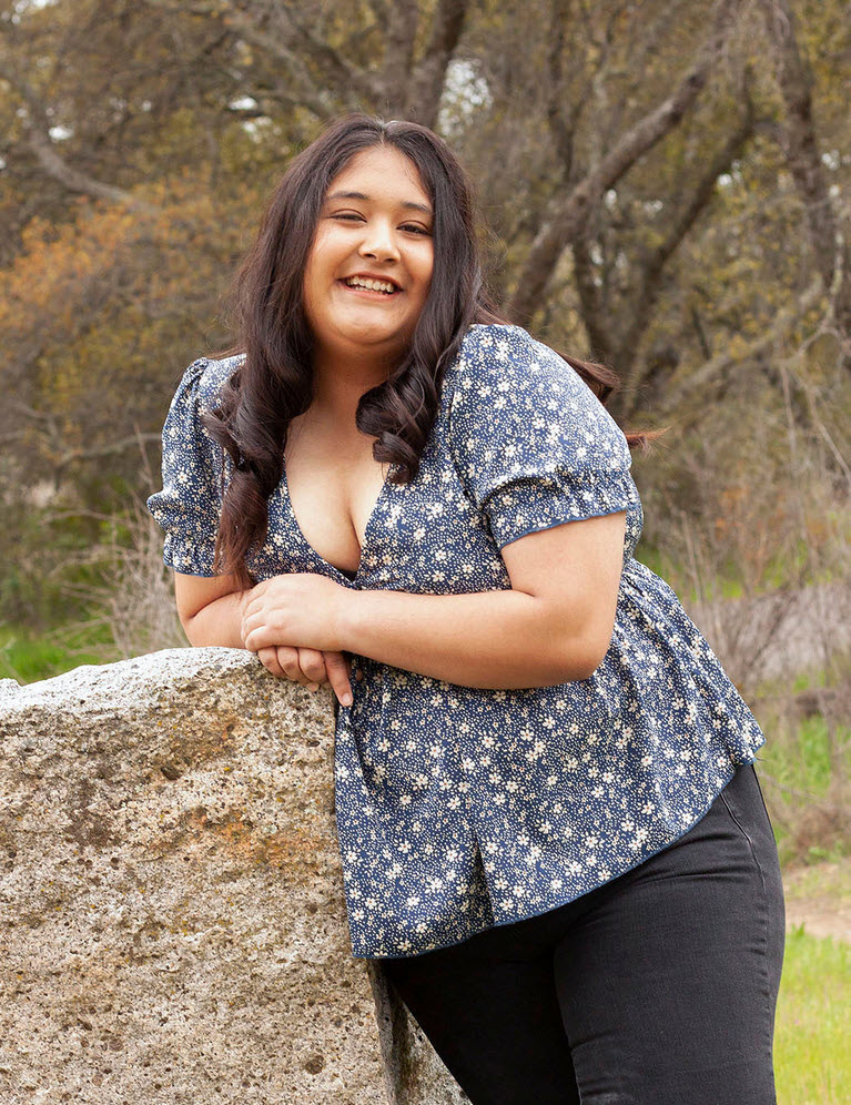 Myla in a blue floral top leaning against a rock